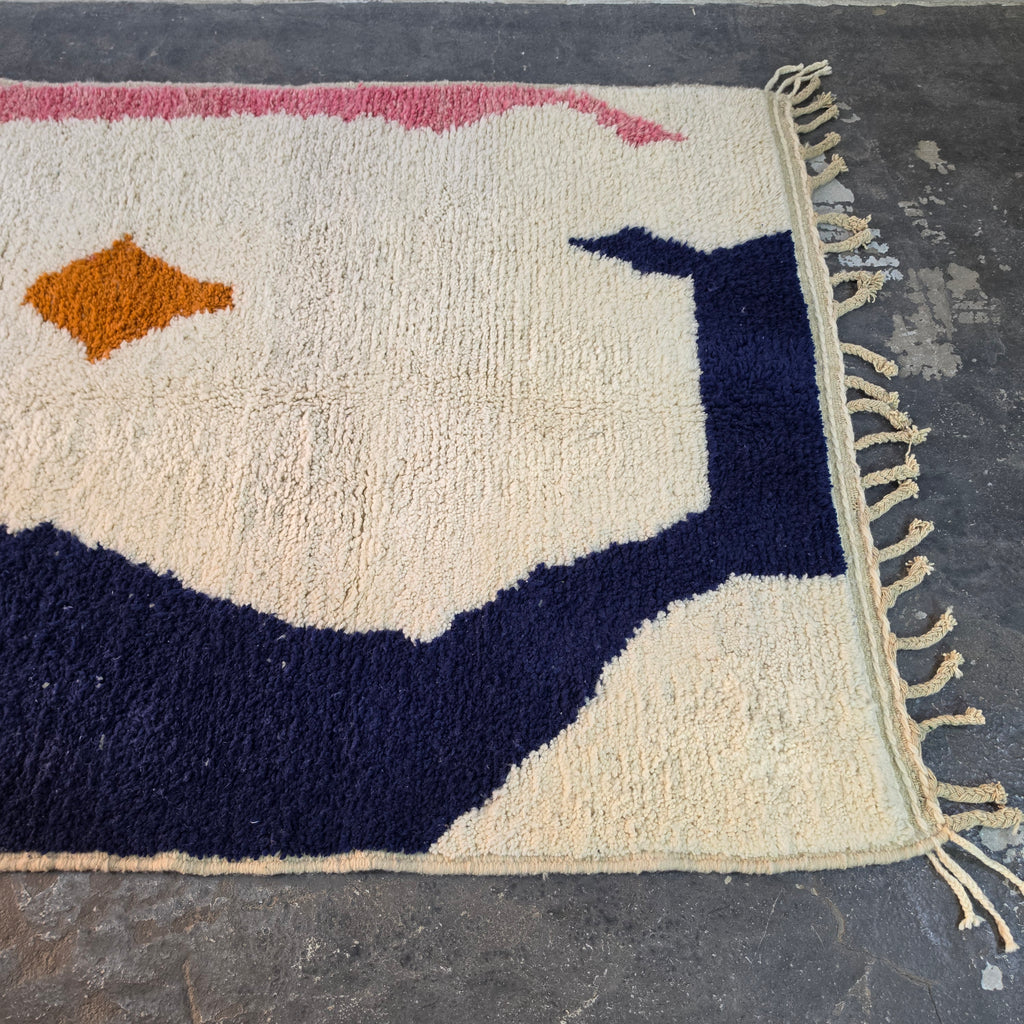 Angled view of the abstract Azilal rug from the other side, with orange diamonds and a navy shape