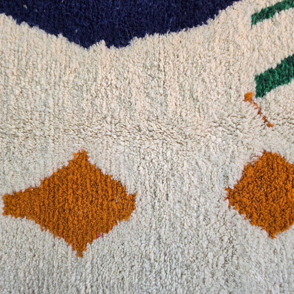 Close-up of burnt orange diamonds and green lines in cream wool