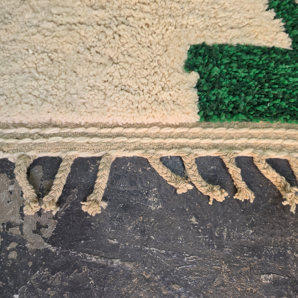 Close-up of the woven edge and hand-tied fringe below an emerald green shape