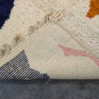 Folded corner of the Azilal rug showing the woven reverse side with navy and pink