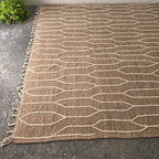 Angled view of the taupe kilim rug showing ivory lines and tasseled edge
