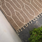 Corner of the taupe kilim rug with ivory lines and hand-finished tassels