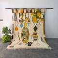 Handmade Moroccan Boujad wool rug hanging on display, cream base with colorful abstract tribal figures in mustard, green, and blue