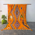 Handmade vibrant orange Moroccan Boujad wool rug hanging on display, with colorful diamond pattern