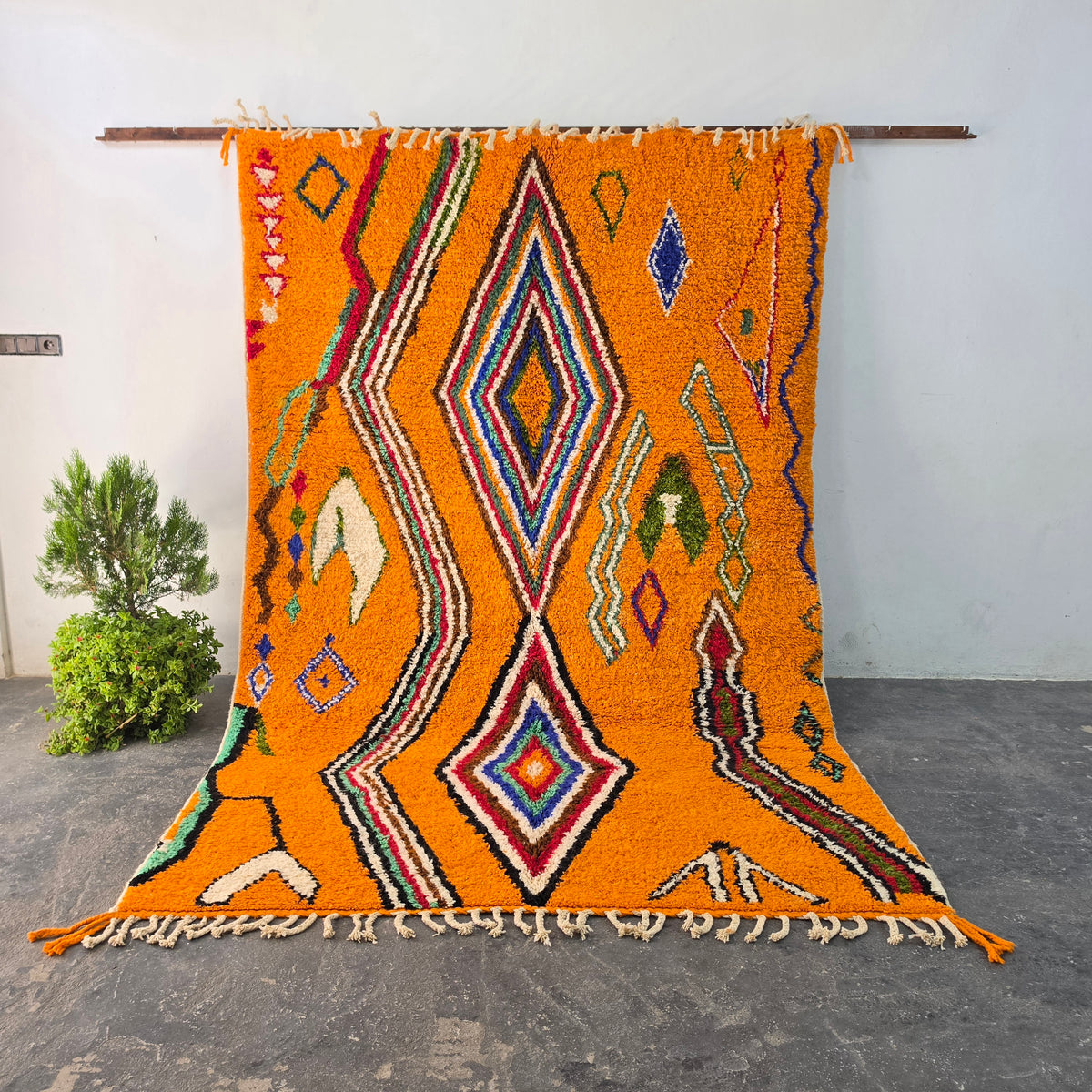 Handmade vibrant orange Moroccan Boujad wool rug hanging on display, with colorful diamond pattern
