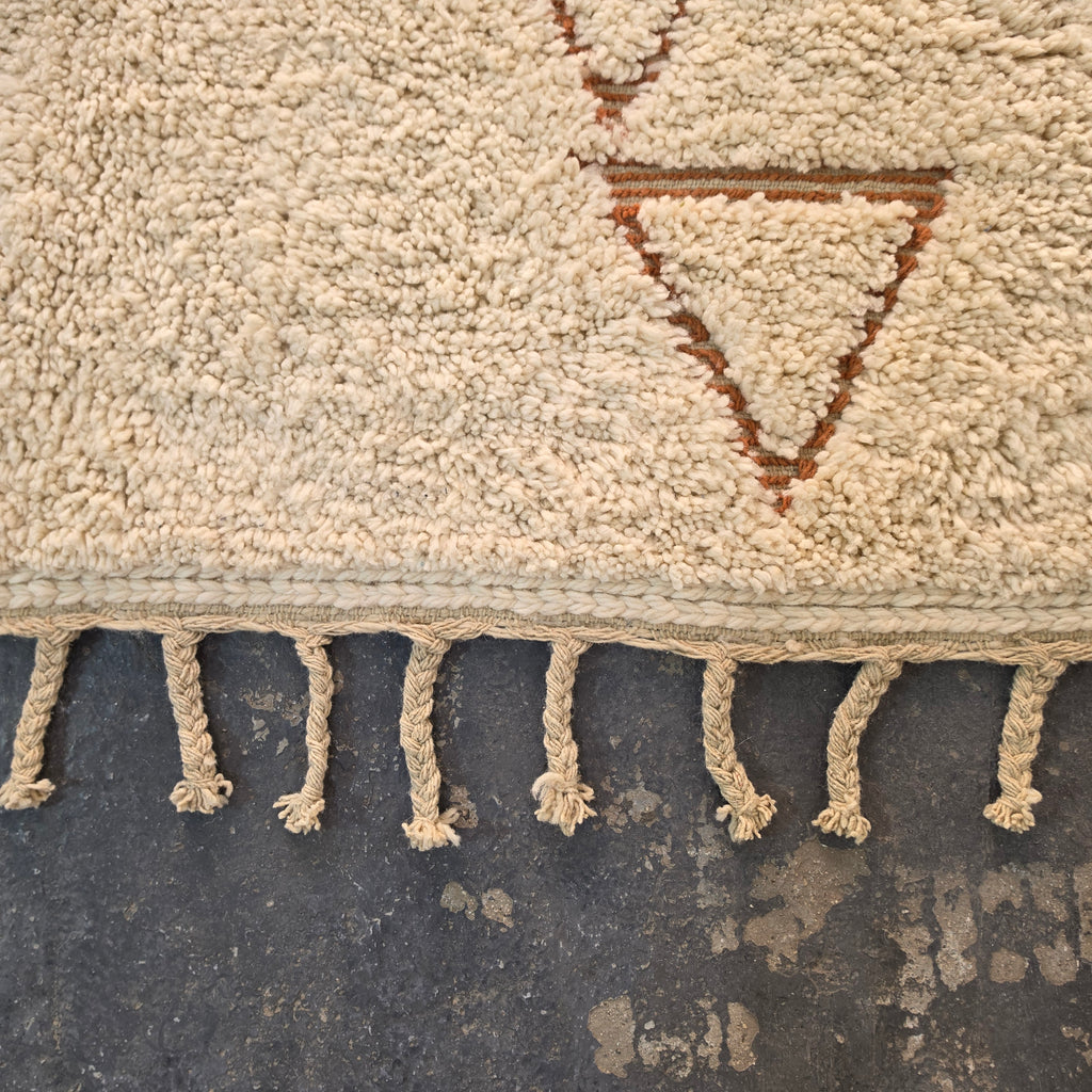 Close-up of hand-tied fringe and rust triangle motif on a Moroccan Berber rug