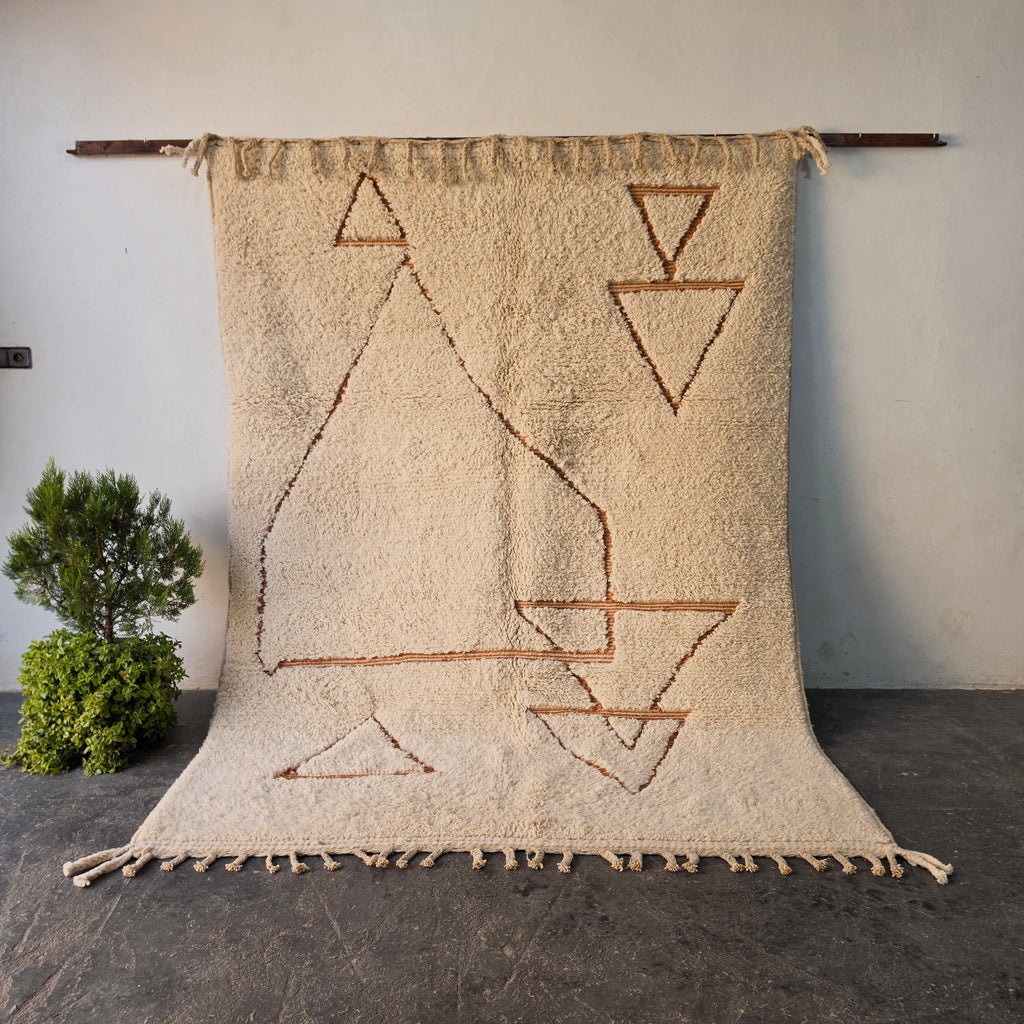 Traditional hand-woven Moroccan Berber rug hanging on display, cream wool with rust triangle and diamond motifs