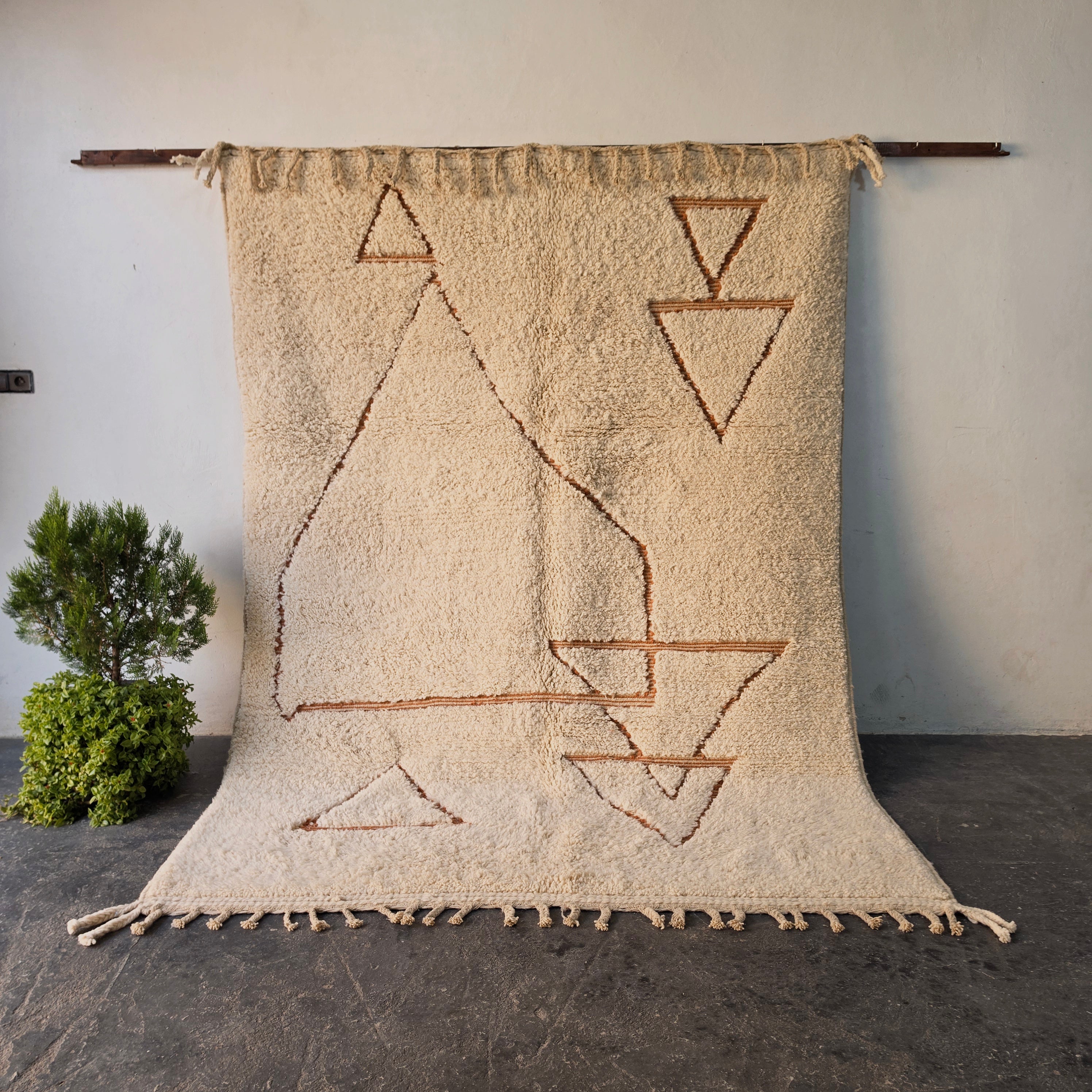 Traditional hand-woven Moroccan Berber rug hanging on display, cream wool with rust triangle and diamond motifs
