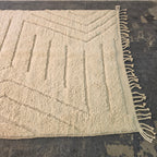 Angled view of the ivory modern boho rug from the other side, with carved lines and fringe