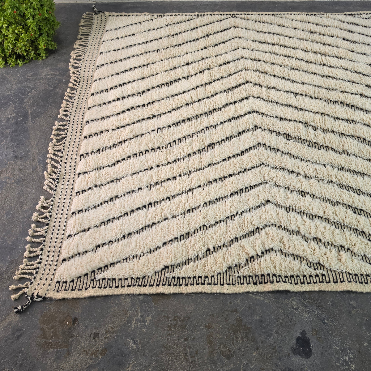 Angled view of Moroccan Beni Ourain rug corner showing wavy chevron pattern and fringe