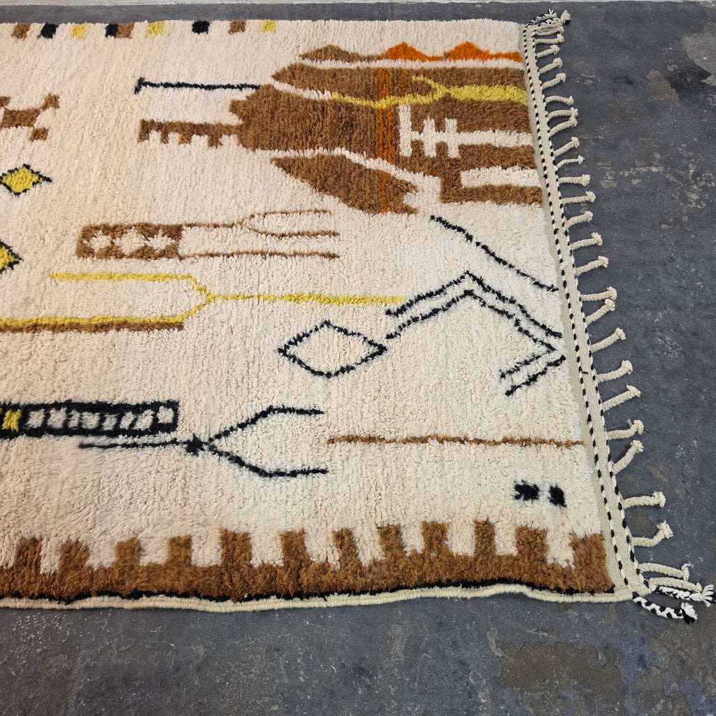 Close-up of Moroccan Berber rug showing brown tribal totem figures and hand-tied fringe