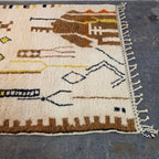 Close-up of Moroccan Berber rug showing brown tribal totem figures and hand-tied fringe