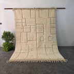 Solid Beni Ourain rug hanging on display, all-ivory wool with carved square relief pattern