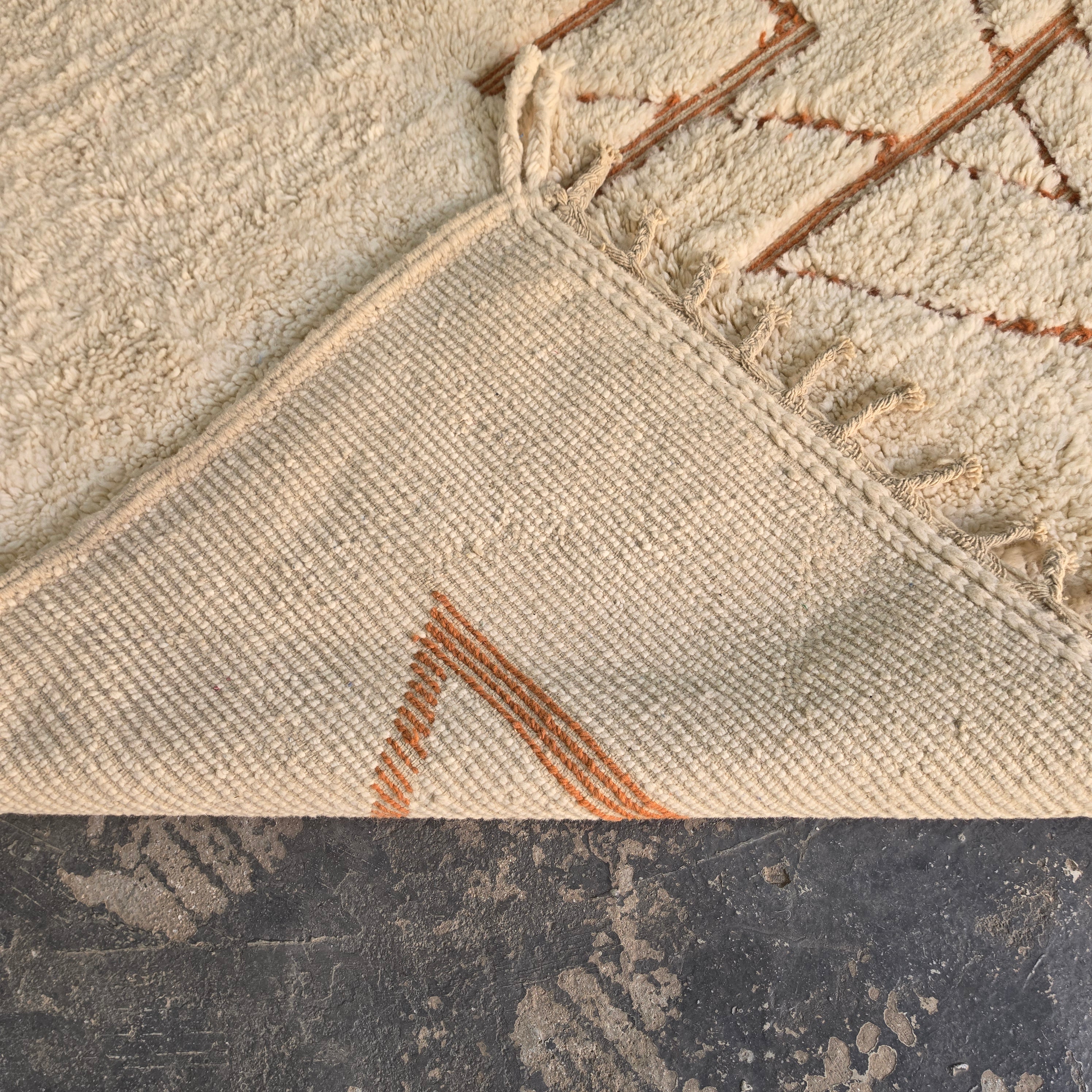 Folded corner of Moroccan Berber rug showing the woven cotton backing and rust line pattern