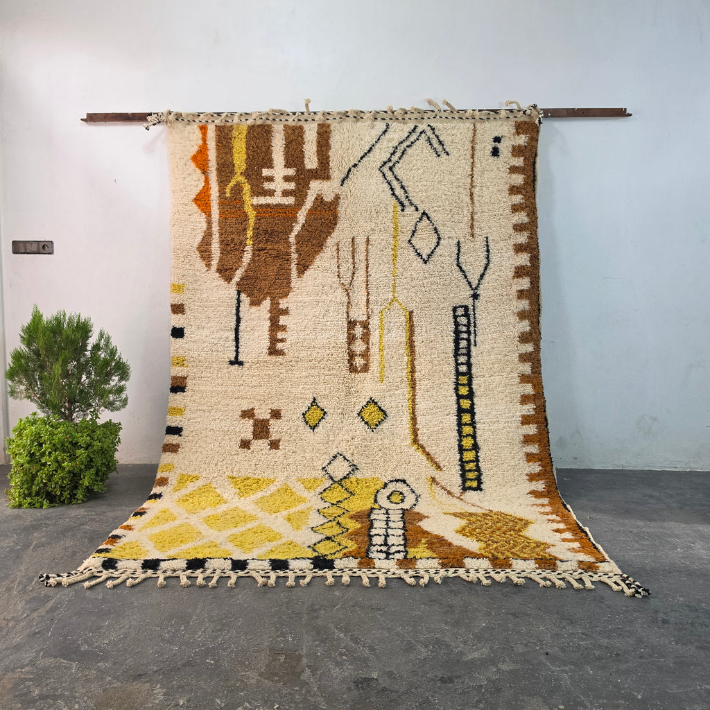 Authentic hand-knotted Moroccan Berber rug hanging on display, ivory wool with brown and mustard tribal symbols