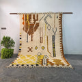 Authentic hand-knotted Moroccan Berber rug hanging on display, ivory wool with brown and mustard tribal symbols