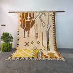 Authentic hand-knotted Moroccan Berber rug hanging on display, ivory wool with brown and mustard tribal symbols