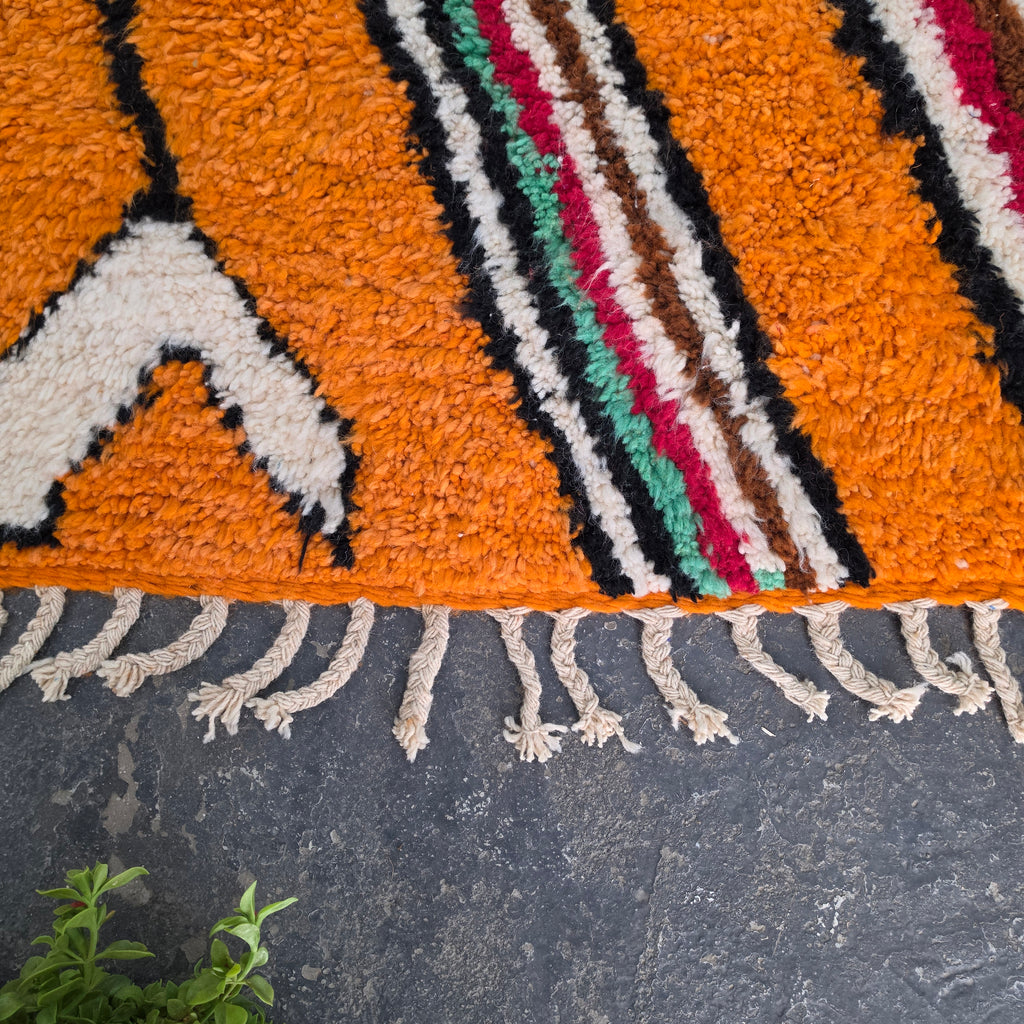 Close-up of striped border and fringe on an orange Moroccan Boujad wool rug