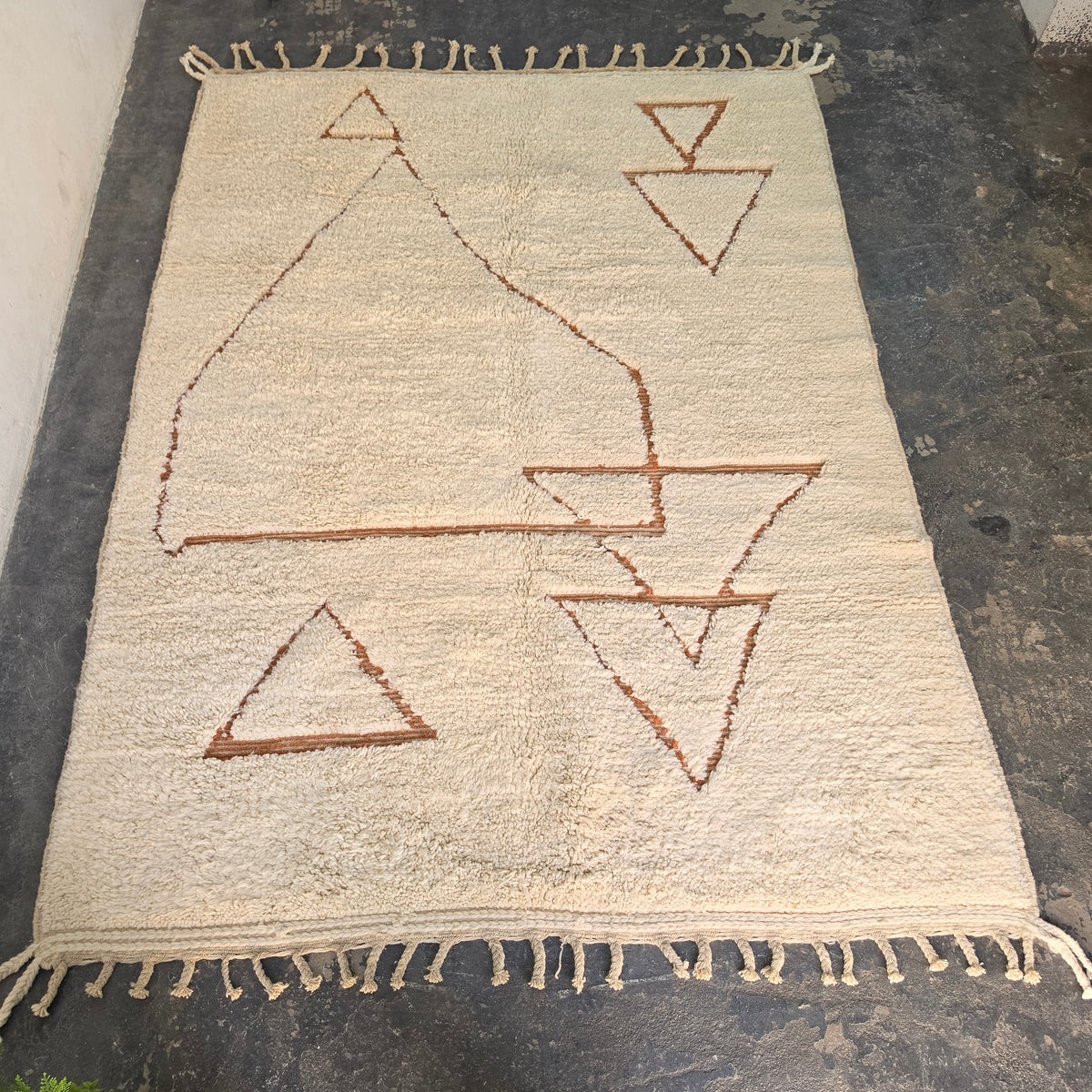 Moroccan Berber rug laid flat, full top-down view of cream pile with rust geometric triangle pattern