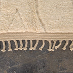 Close-up of the woven edge and hand-tied fringe of the solid ivory Beni Ourain rug