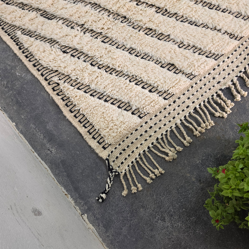 Close-up of Moroccan Beni Ourain rug corner showing fringe tassels and chevron edge pattern