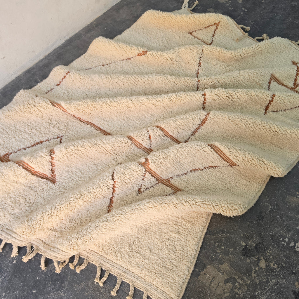 Moroccan Berber rug folded in soft waves showing cream wool and rust triangle motifs