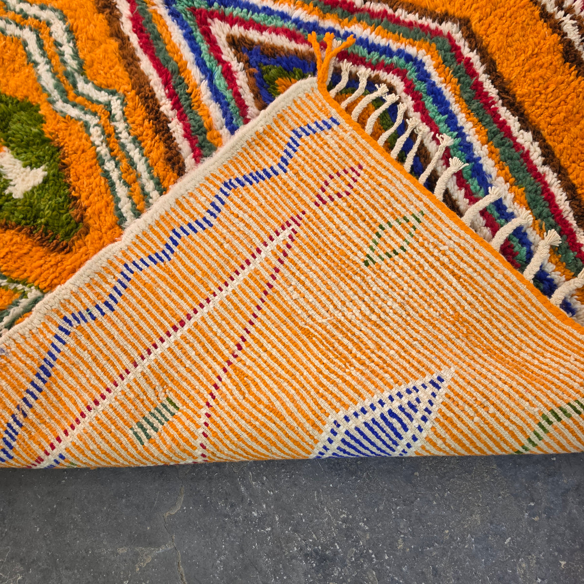 Folded corner of orange Moroccan Boujad rug showing the woven flat-weave pattern on the reverse side