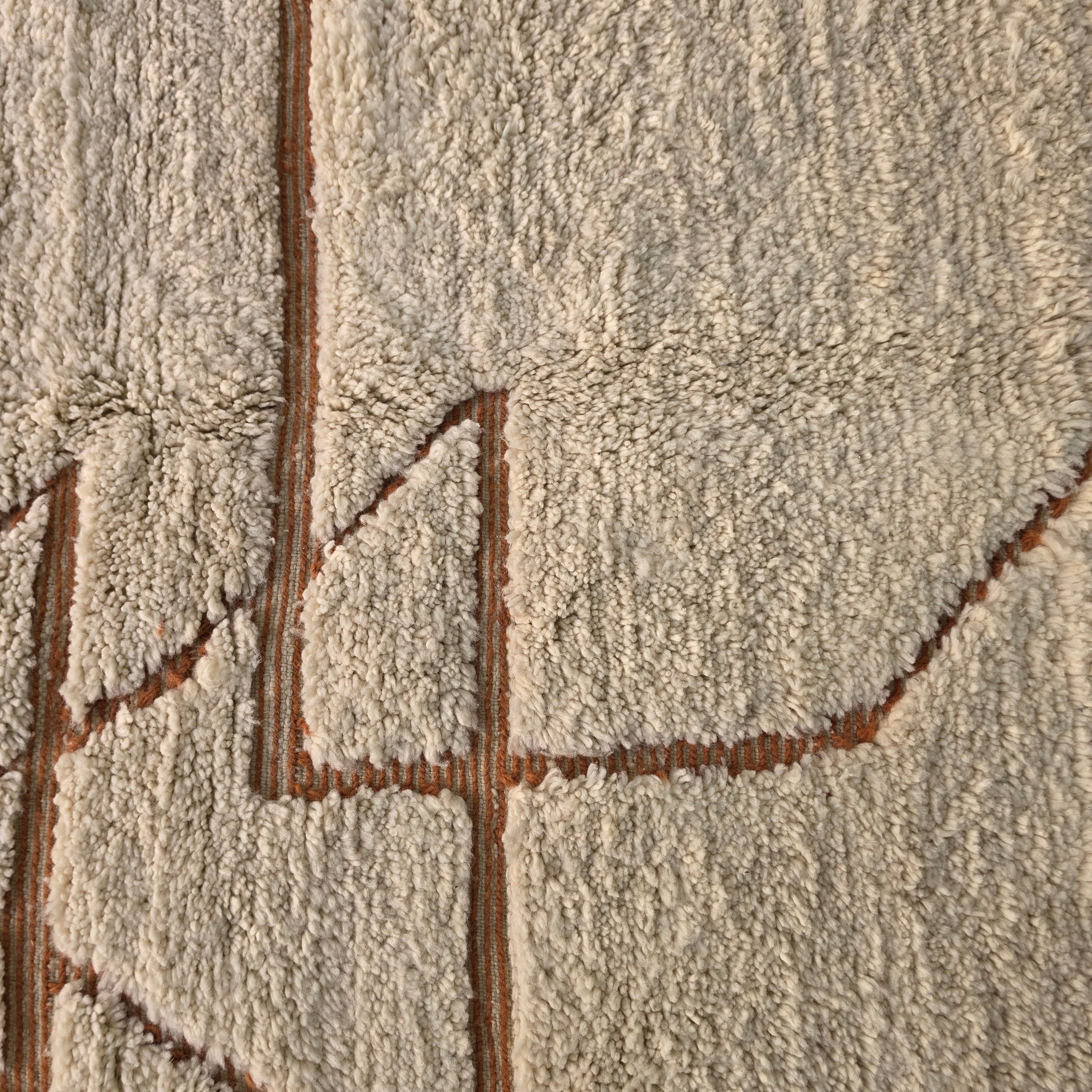 Macro close-up of rust-colored geometric pattern woven into cream wool pile