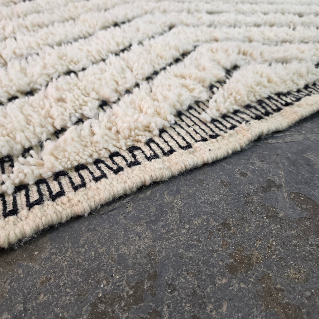 Close-up of plush ivory wool pile texture with black chevron lines on a Beni Ourain rug