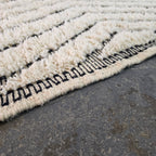 Close-up of plush ivory wool pile texture with black chevron lines on a Beni Ourain rug