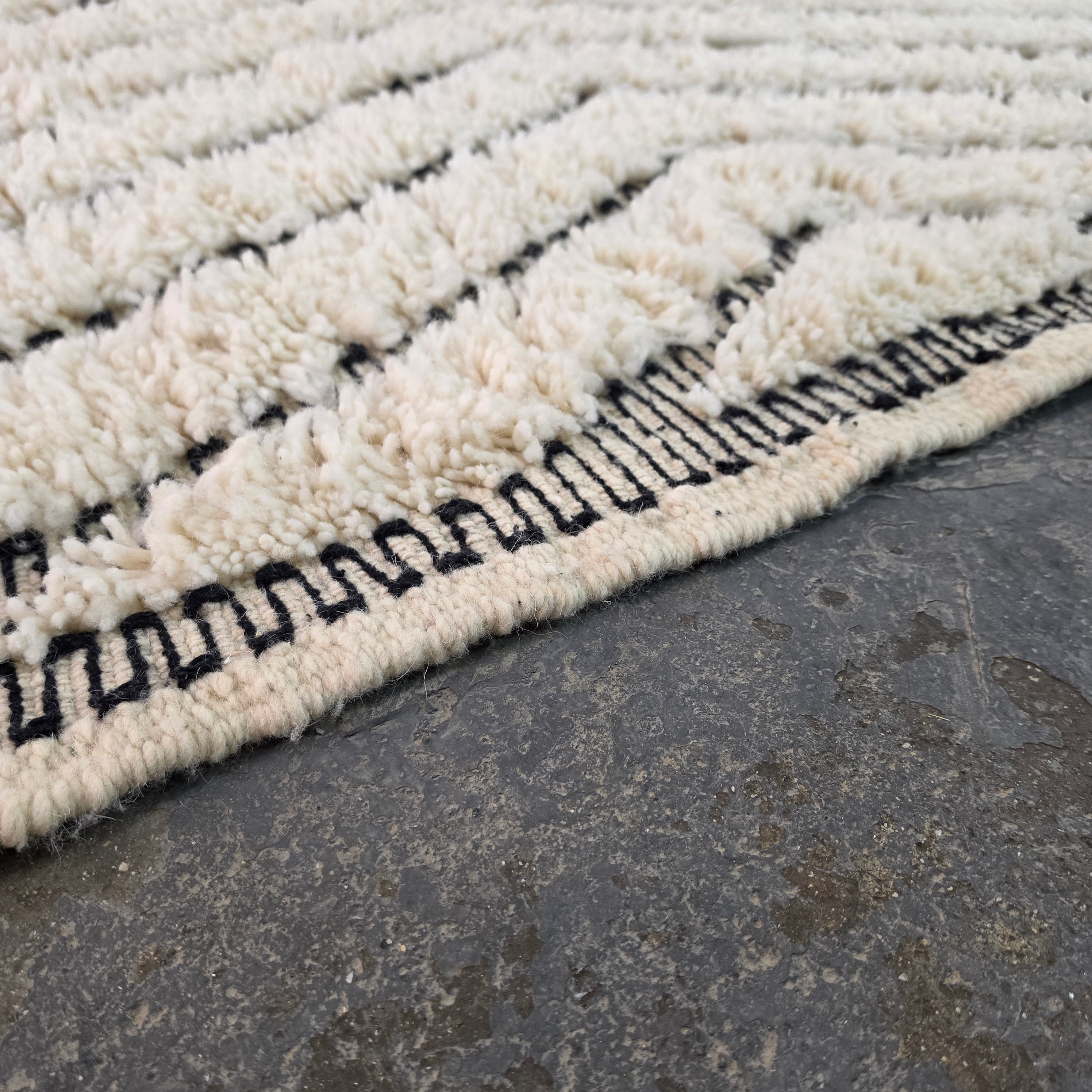 Close-up of plush ivory wool pile texture with black chevron lines on a Beni Ourain rug