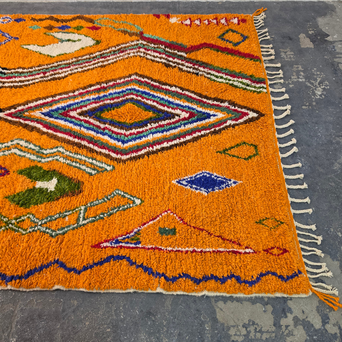 Angled view of orange Moroccan Boujad rug showing diamond motifs and fringed edge