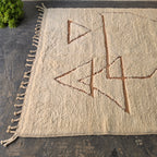 Angled view of cream Moroccan Berber rug showing rust triangle motifs and fringed edge