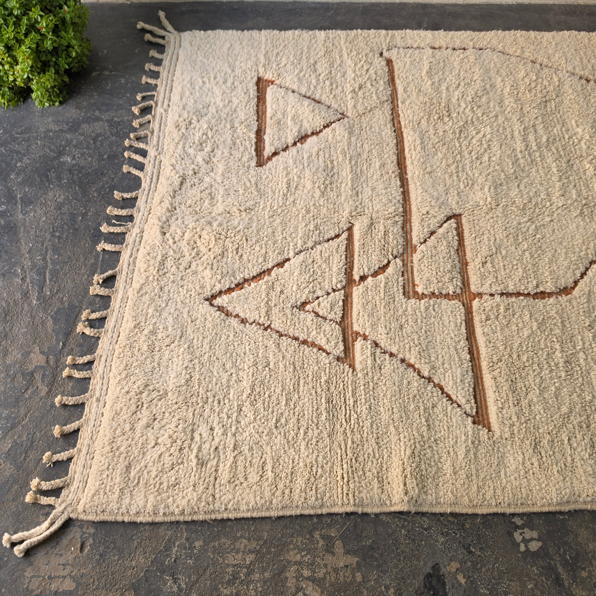 Angled view of cream Moroccan Berber rug showing rust triangle motifs and fringed edge