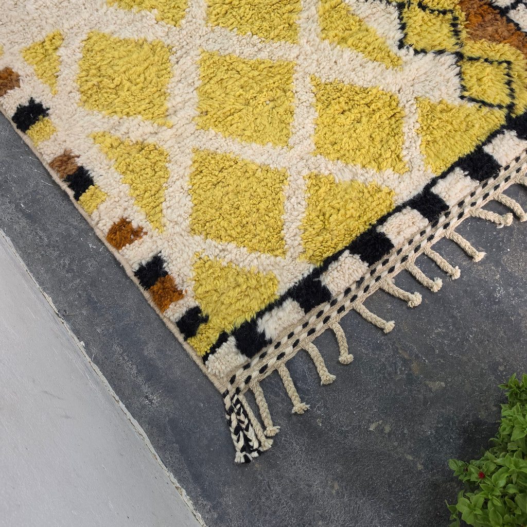 Close-up corner of Moroccan Berber rug with yellow diamond pattern and cream fringe tassels