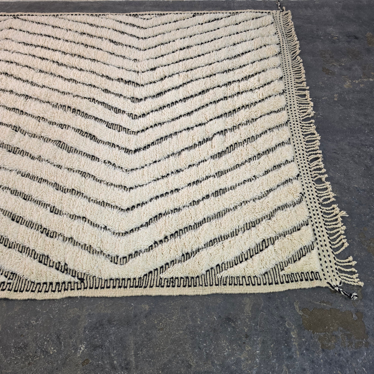 Close angled view of Moroccan Beni Ourain rug corner with chevron pattern and hand-tied fringe