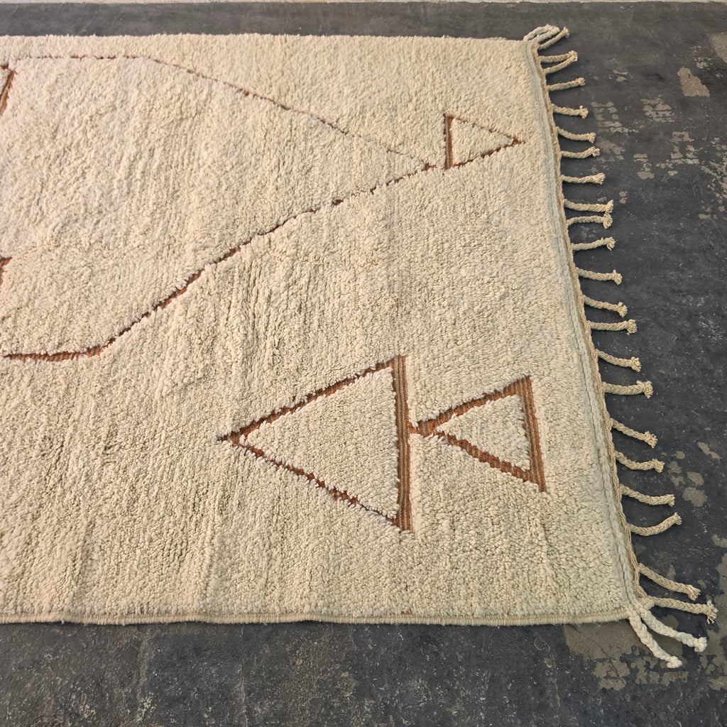 Close-up corner of Moroccan Berber rug showing plush cream wool pile and rust triangle design