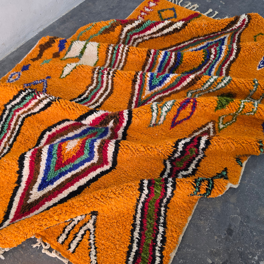 Orange Moroccan Boujad rug folded in soft waves showing colorful diamond pattern
