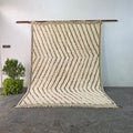 Handmade Moroccan Beni Ourain wool rug hanging on display, ivory wool with black wavy chevron pattern